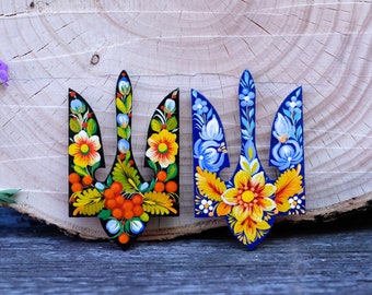 May include: Two wooden Ukrainian tridents painted with colorful floral designs. One trident is painted in blue, yellow, and white, while the other is painted in black, orange, yellow, and green.