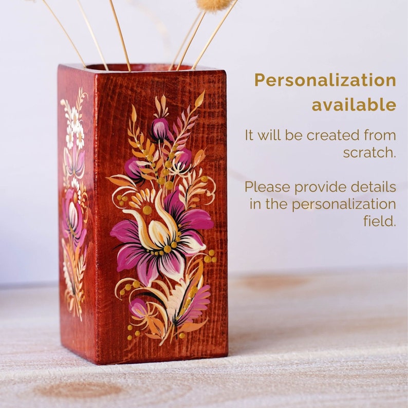 Puede incluir: Un jarr&oacute;n de madera con un dise&ntilde;o floral pintado a mano en tonos de rosa, amarillo y dorado. El jarr&oacute;n est&aacute; hecho de madera y tiene una forma cuadrada. Es un art&iacute;culo personalizado y se puede personalizar con diferentes dise&ntilde;os.