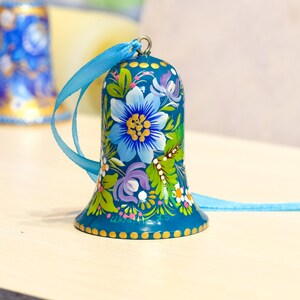 May include: A teal blue bell ornament with a floral design painted on it. The bell has a blue ribbon attached to the top.