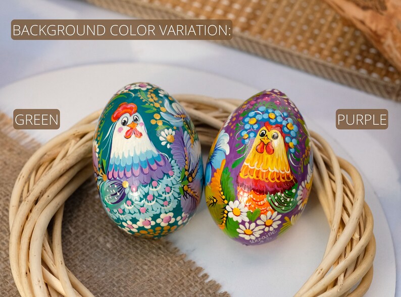 May include: Two hand-painted Easter eggs featuring a chicken design. One egg is green with a purple chicken, while the other is purple with a yellow chicken. Both eggs are decorated with white flowers and green leaves.
