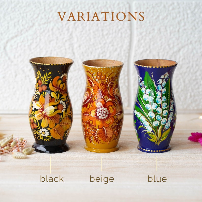 May include: Three wooden vases with hand-painted floral designs. The vases are in black, beige, and blue.