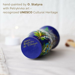 May include: A blue vase hand-painted with a floral design in yellow, green, and blue. The vase is labeled "ukraine Petrykivka art.. O. Statyva" and is recognized as a UNESCO Cultural Heritage.