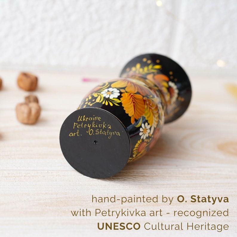 May include: Black and gold hand-painted vase with floral designs. The vase is decorated with the text "Ukraine Petrykivka art. O. Statyva" and "hand-painted by O. Statyva with Petrykivka art - recognized UNESCO Cultural Heritage".