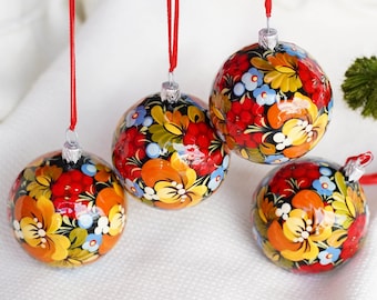 May include: Four round Christmas ornaments with a floral design. The ornaments are painted with red, yellow, blue, and orange flowers on a black background. Each ornament hangs from a red ribbon.