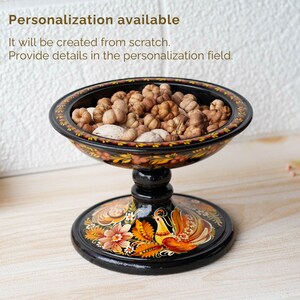 May include: A black wooden bowl with a painted floral design and a bird on the base. The bowl is filled with dried flower buds.