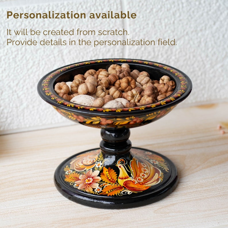 May include: A black wooden bowl with a painted floral design and a bird on the base. The bowl is filled with dried flower buds.