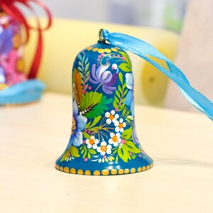 May include: A blue bell with a floral design painted on it. The bell has a gold trim and a blue ribbon attached to it.