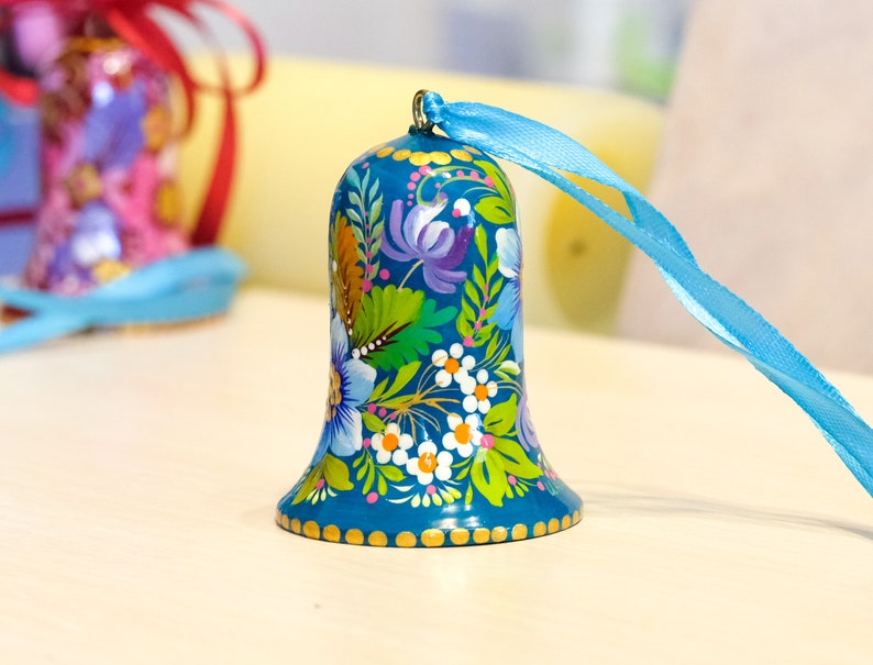 May include: A blue bell with a floral design painted on it. The bell has a gold trim and a blue ribbon attached to it.