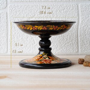 May include: Black wooden pedestal bowl with hand-painted floral designs in orange, yellow, and red. The bowl is 7.3 inches in diameter and 5.1 inches tall.