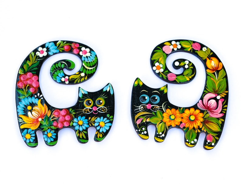 May include: Two black wooden cat figurines with colorful floral designs painted on them. The cats are curled up with their tails forming a circle.