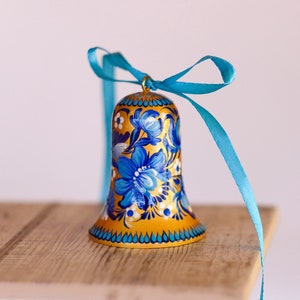 Puede incluir: Una campana dorada con dise&ntilde;os florales azules y blancos y una cinta turquesa.