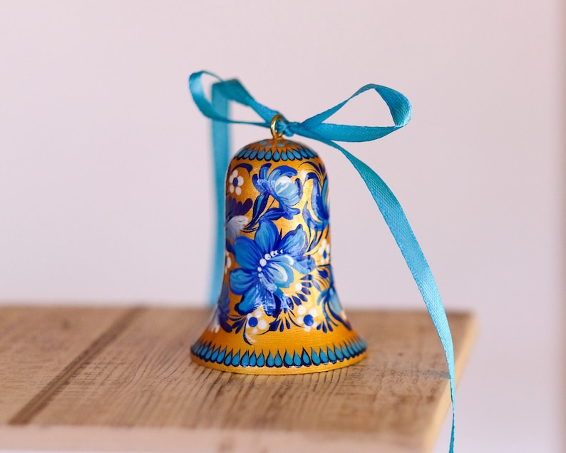 Puede incluir: Una campana dorada con dise&ntilde;os florales azules y blancos y una cinta turquesa.