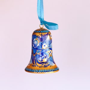 Puede incluir: Un adorno de campana pintado en azul y dorado con dise&ntilde;os florales. La campana tiene una cinta azul atada a la parte superior y las palabras "Ucrania" y "1.5" escritas en la parte inferior.