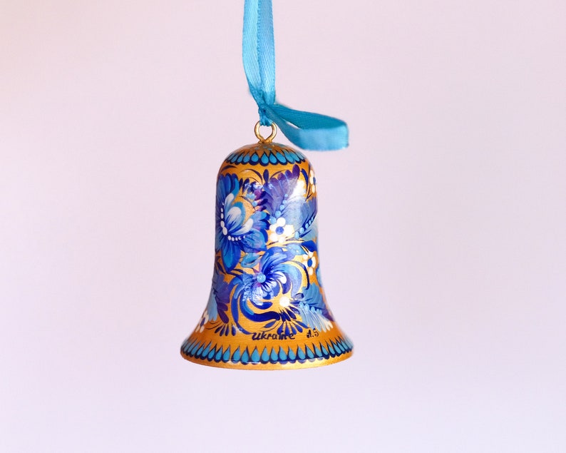 Puede incluir: Un adorno de campana pintado en azul y dorado con dise&ntilde;os florales. La campana tiene una cinta azul atada a la parte superior y las palabras "Ucrania" y "1.5" escritas en la parte inferior.