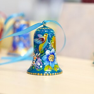 May include: A blue bell ornament with a painted design of flowers and birds. The bell has a gold trim and is tied with a blue ribbon.