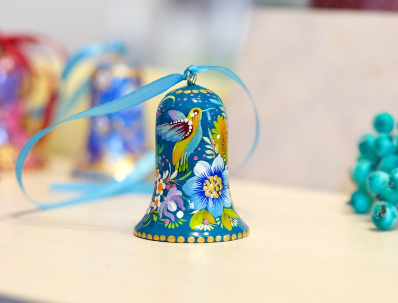 May include: A blue bell ornament with a painted design of flowers and birds. The bell has a gold trim and is tied with a blue ribbon.