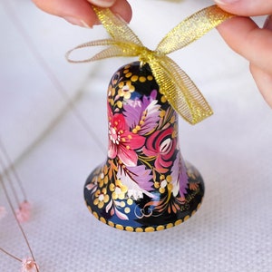May include: A black bell ornament with a gold ribbon. The bell is painted with a floral design in shades of pink, purple, and gold.