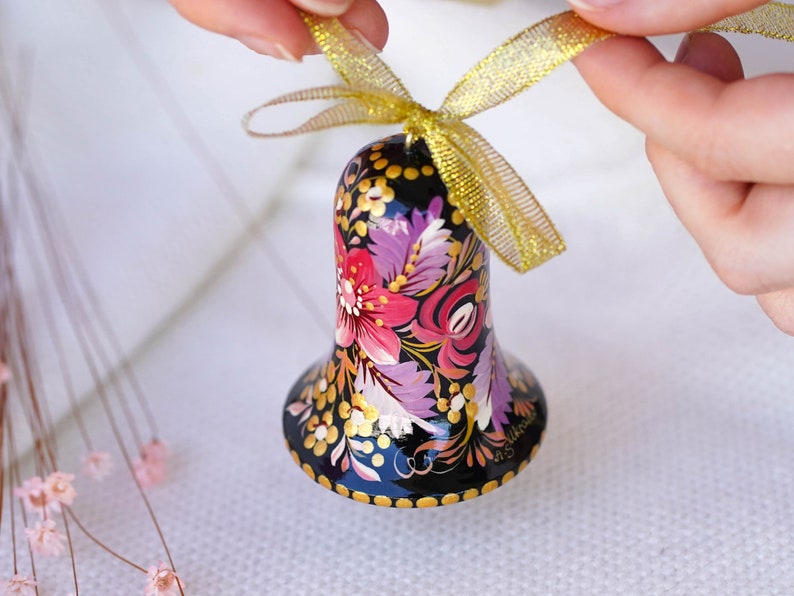 May include: A black bell ornament with a gold ribbon. The bell is painted with a floral design in shades of pink, purple, and gold.