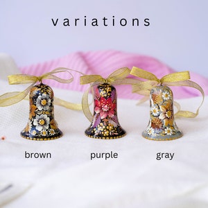 May include: Three hand-painted wooden bells with floral designs. The bells are black, purple, and gray with gold accents. The bells are tied with gold ribbon.