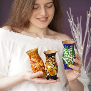 May include: Three hand-painted wooden vases with floral designs. The vases are blue, yellow, and black with white floral patterns.