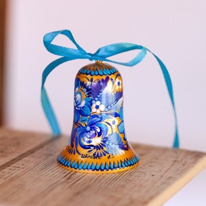 Puede incluir: Una campana azul y dorada con un dise&ntilde;o floral y la palabra "Ucrania" pintada en ella. La campana est&aacute; atada con una cinta azul.