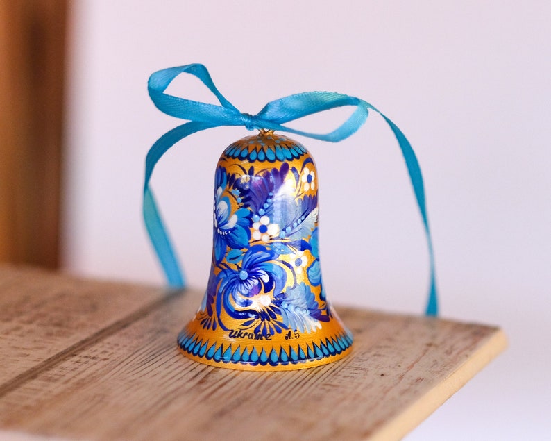 Puede incluir: Una campana azul y dorada con un dise&ntilde;o floral y la palabra "Ucrania" pintada en ella. La campana est&aacute; atada con una cinta azul.