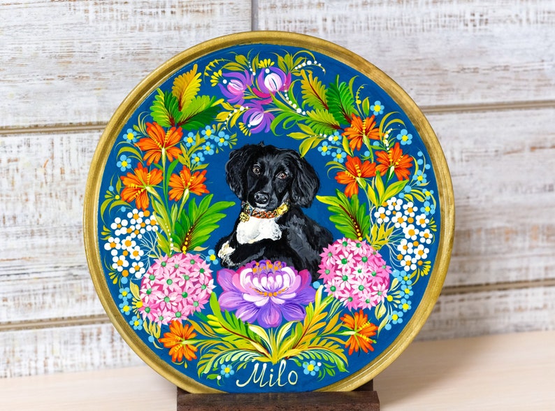 Puede incluir: Un plato de cer&aacute;mica pintado a mano con un retrato de un perro blanco y negro rodeado de flores coloridas. El plato tiene un borde dorado y el nombre del perro, "Milo", est&aacute; escrito en cursiva en la parte inferior.