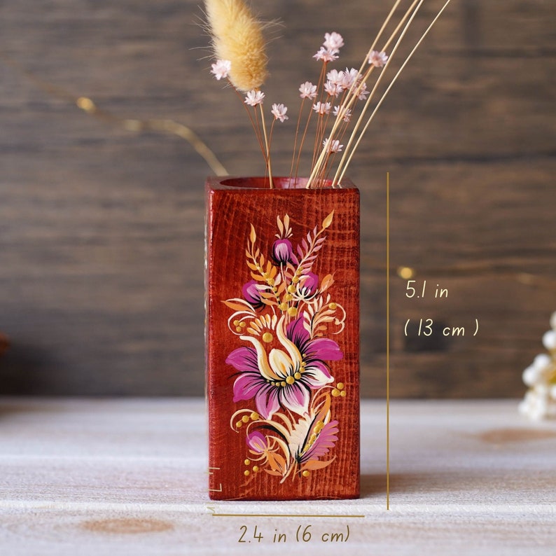 Puede incluir: Un jarr&oacute;n de madera pintado a mano con un dise&ntilde;o floral en tonos rosa, amarillo y naranja. El jarr&oacute;n mide 13 cm de alto y 6 cm de ancho.
