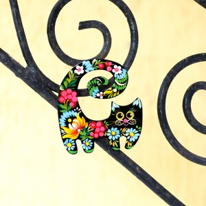 May include: A black wooden cat figurine with a floral design painted on it. The cat is sitting on a black metal railing.