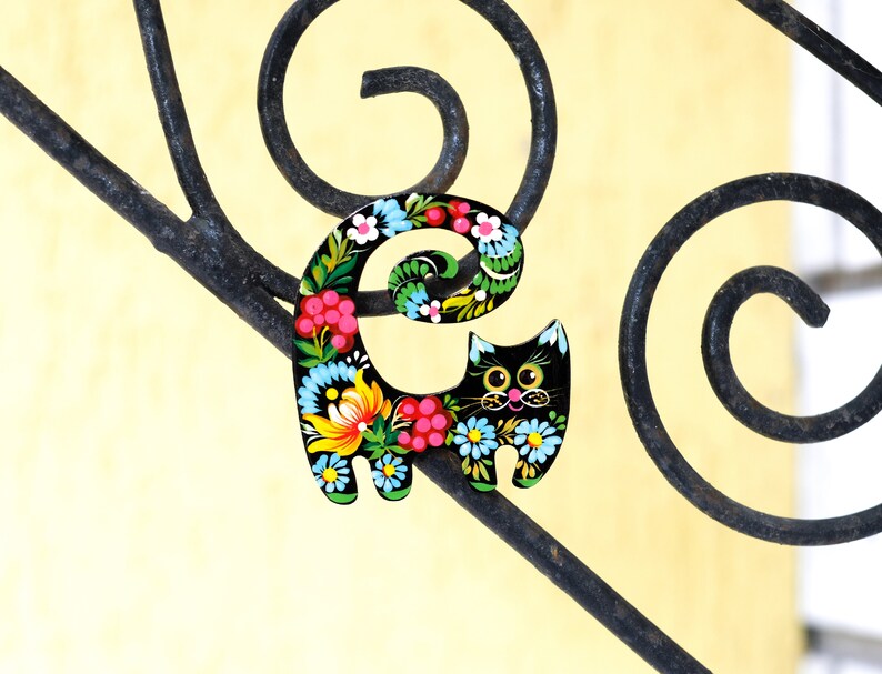 May include: A black wooden cat figurine with a floral design painted on it. The cat is sitting on a black metal railing.