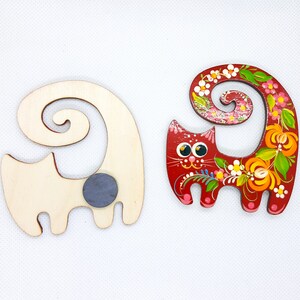 May include: Two wooden cat figurines. One is painted red with floral designs and the other is unpainted with a grey magnet on the back.