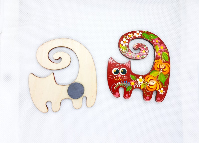 May include: Two wooden cat figurines. One is painted red with floral designs and the other is unpainted with a grey magnet on the back.