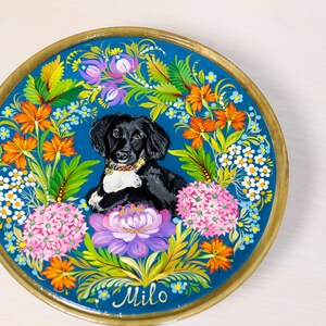 Puede incluir: Un plato redondo de madera con fondo azul y un dise&ntilde;o floral pintado. Un perro blanco y negro est&aacute; en el centro del plato, rodeado de flores. El nombre del perro, "Milo", est&aacute; escrito en cursiva en la parte inferior del plato.