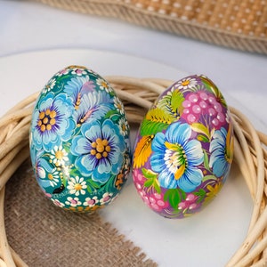 May include: Two hand-painted Easter eggs with floral designs. One egg is blue with yellow and white flowers, the other is purple with pink and green flowers.