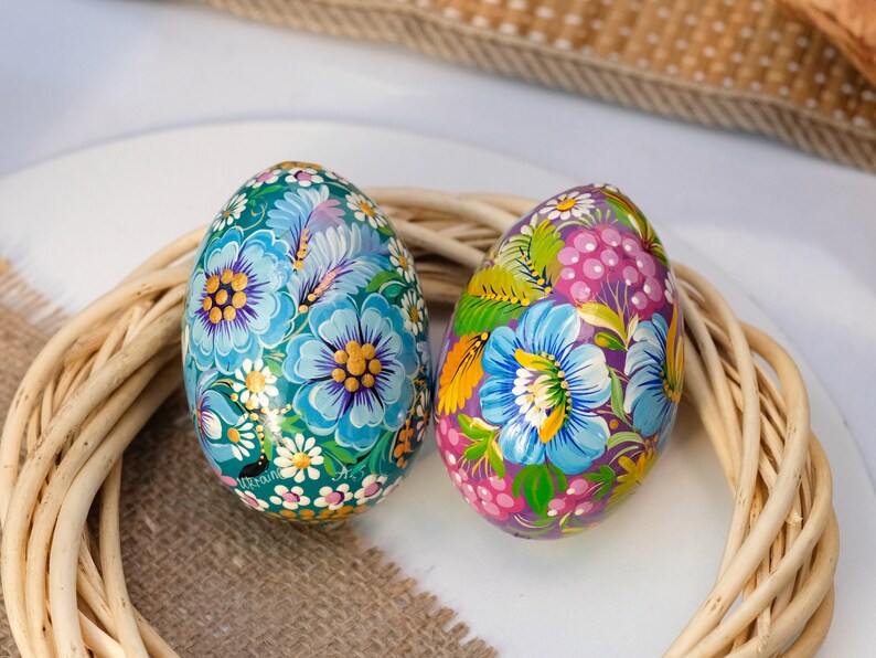 May include: Two hand-painted Easter eggs with floral designs. One egg is blue with yellow and white flowers, the other is purple with pink and green flowers.