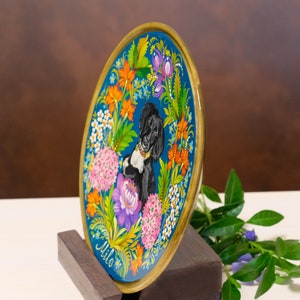 Puede incluir: Un plato redondo de madera con fondo azul y un perro blanco y negro pintado en el centro. El plato est&aacute; decorado con flores de colores y el nombre "Milo" est&aacute; pintado en la parte inferior.