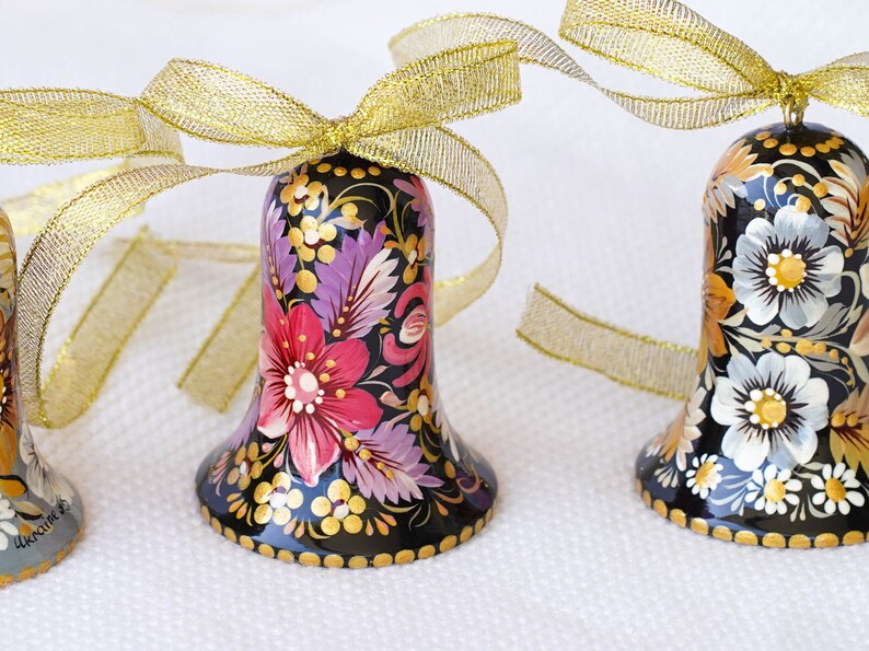 May include: Three black bells with gold ribbon bows. Each bell is hand-painted with colorful floral designs. The bells are a traditional Russian folk art.