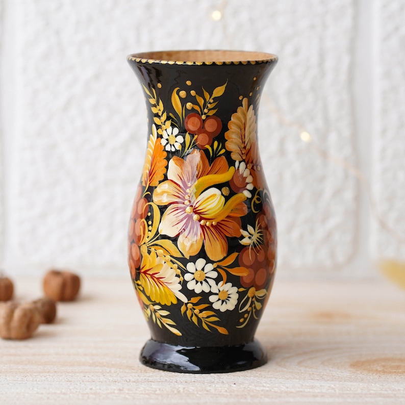 May include: A black wooden vase with a floral design painted in shades of orange, yellow, and white. The vase has a rounded body and a flared top.