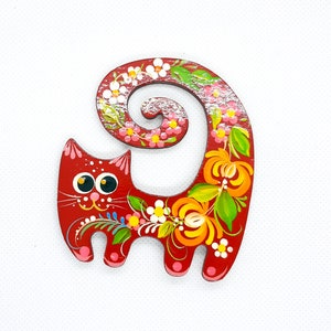 May include: A red wooden cat figurine with a curled tail. The cat is painted with colourful flowers and leaves in a folk art style.