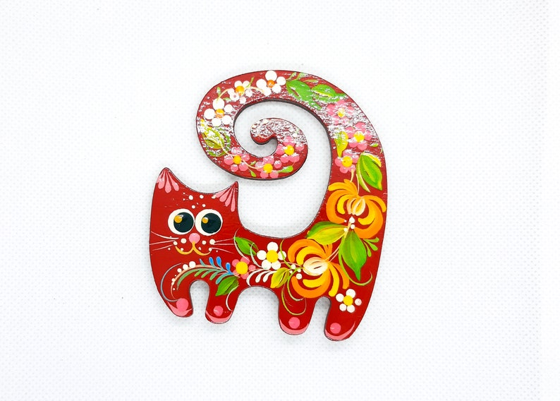 May include: A red wooden cat figurine with a curled tail. The cat is painted with colourful flowers and leaves in a folk art style.