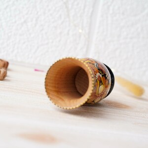 May include: A wooden cup with a black and yellow floral design. The cup is empty and the inside is visible.