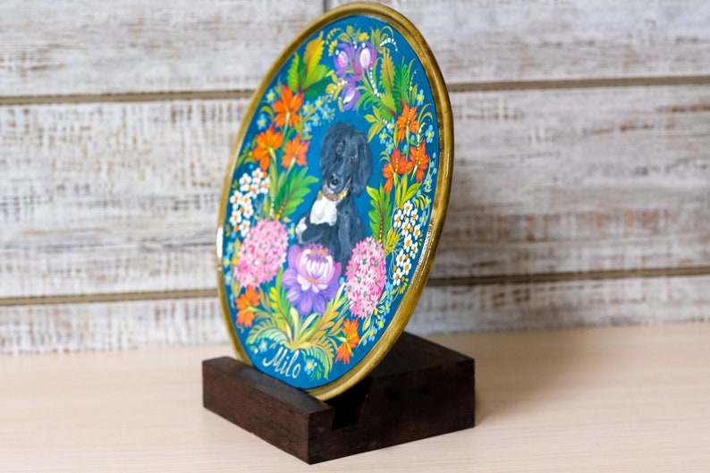 Puede incluir: Un plato redondo pintado en azul y dorado con un retrato de perro negro y blanco en el centro. El plato est&aacute; rodeado de flores coloridas y el nombre "Milo" est&aacute; escrito en la parte inferior.