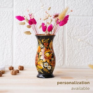 May include: A black vase with a floral design painted in yellow, orange, and white. The vase is filled with dried flowers in shades of pink and beige.