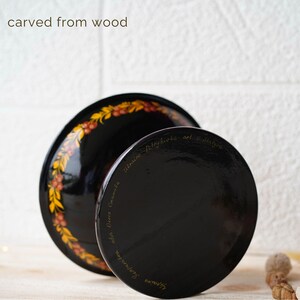 May include: A black wooden bowl with a gold and red floral design. The bowl is carved from wood and has a stand. The bottom of the bowl is inscribed with the text "ukraїns'ka  petrykivka art &  sl'stva  cel'm.  Olena  Gromula  Svitlana".