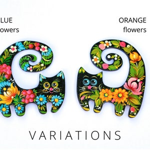 May include: Two black wooden cat figurines with painted floral designs. One cat has blue flowers and the other has orange flowers. The text "BLUE flowers" and "ORANGE flowers" is above each cat.