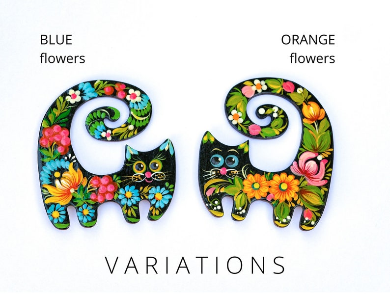 May include: Two black wooden cat figurines with painted floral designs. One cat has blue flowers and the other has orange flowers. The text "BLUE flowers" and "ORANGE flowers" is above each cat.