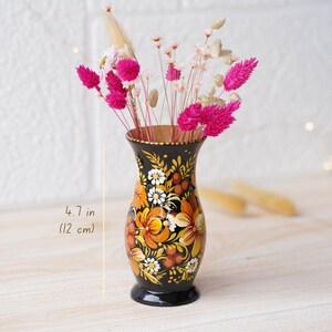 May include: A black and gold hand-painted vase with floral designs. The vase is 4.7 inches (12 cm) tall and is filled with dried flowers.