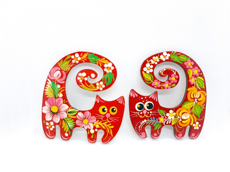 May include: Two red wooden cats with curled tails painted with colourful flowers and swirls. The cats have black eyes and white pupils.