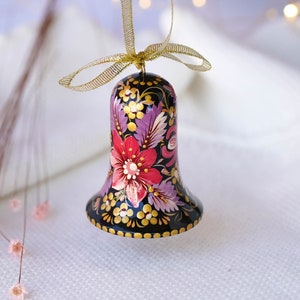 May include: A black bell ornament with a gold ribbon and a hand-painted floral design in shades of pink, purple, and gold.