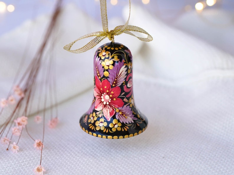 May include: A black bell ornament with a gold ribbon and a hand-painted floral design in shades of pink, purple, and gold.